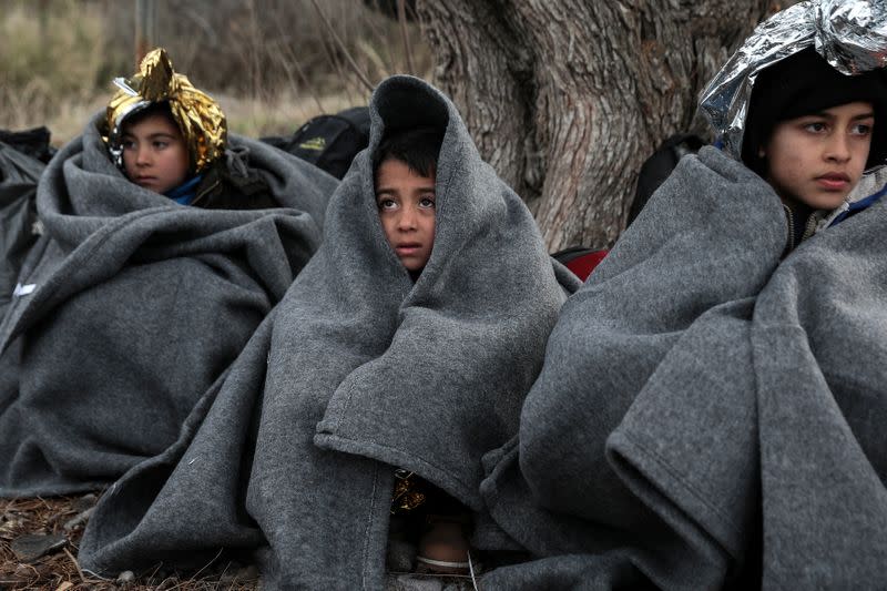 Children are covered with blankets and thermal blankets after migrants from Afghanistan arrived on a dinghy on a beach near the village of Skala Sikamias on the island of Lesbos