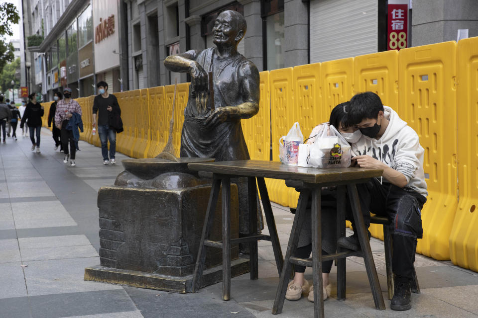 In this Wednesday, April 8, 2020, photo, a couple share a quiet moment on the streets of Wuhan in central China's Hubei province. Released from their apartments after a 2 1/2-month quarantine, residents of the city where the coronavirus pandemic began are cautiously returning to shopping and strolling in the street but say they still go out little and keep children home while they wait for schools to reopen. (AP Photo/Ng Han Guan)