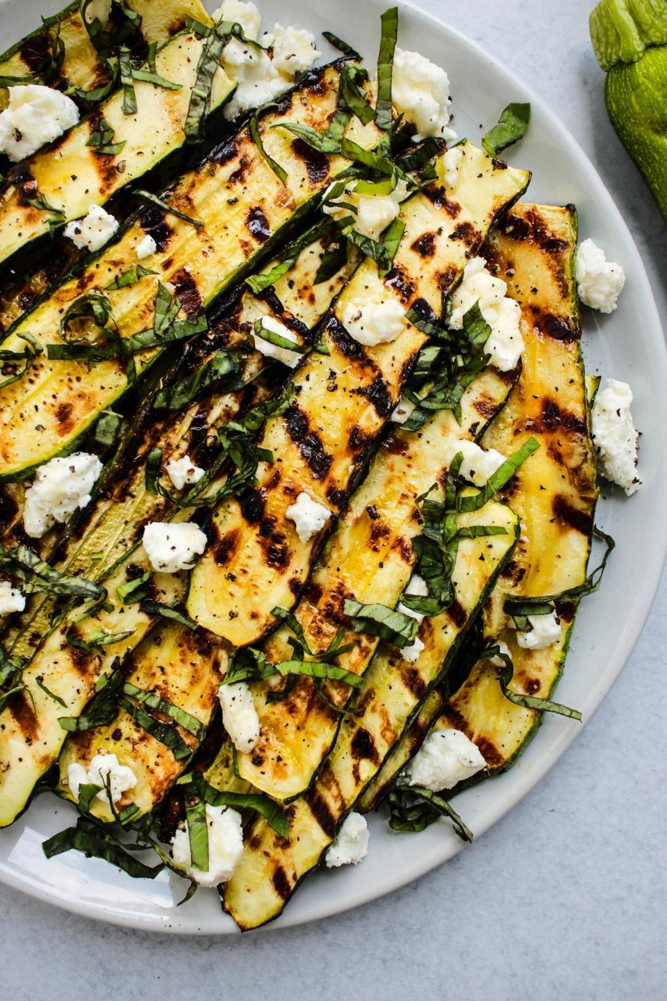 Slices of grilled zucchini topped with herbs and cheese on a white plate