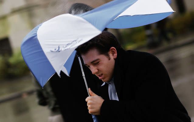 A man struggles to hold an umbrella admidst heavy winds and rain. Source: Getty Images