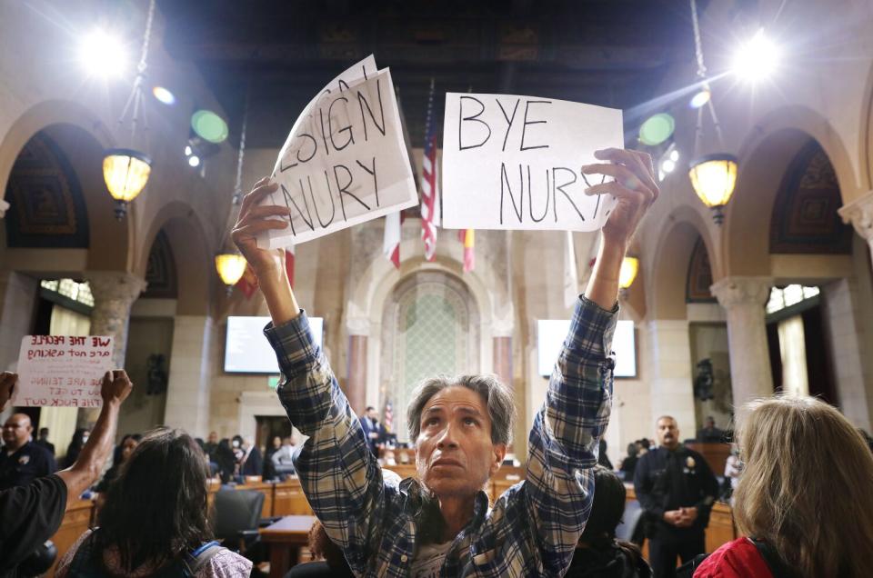 A man with other protesters holds signs reading "Resign Nury" and "Bye Nury"