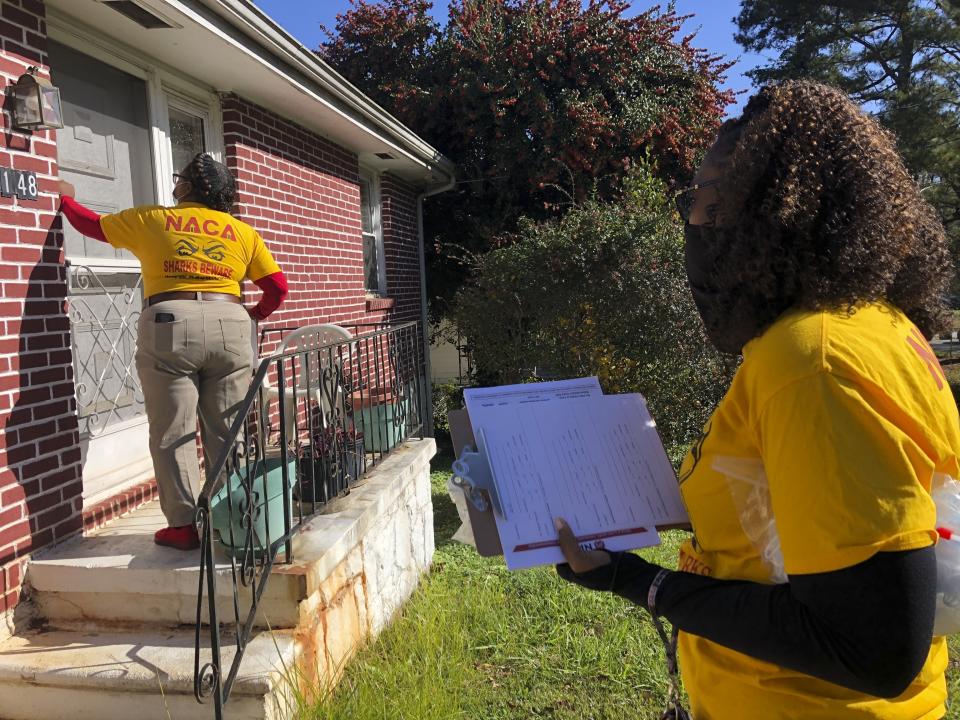 Phyllis Morrow knocks on a door in Decatur, Ga. on Friday, Nov. 27, 2020. Morrow and Jocelyn Johnson, foreground, are going door to door for the Neighborhood Assistance Corporation of America to encourage people to vote for Democrats Jon Ossoff and Raphael Warnock in Georgia’s pivotal Jan. 5 runoff elections for U.S. Senate. (AP Photo/Sudhin Thanawala)