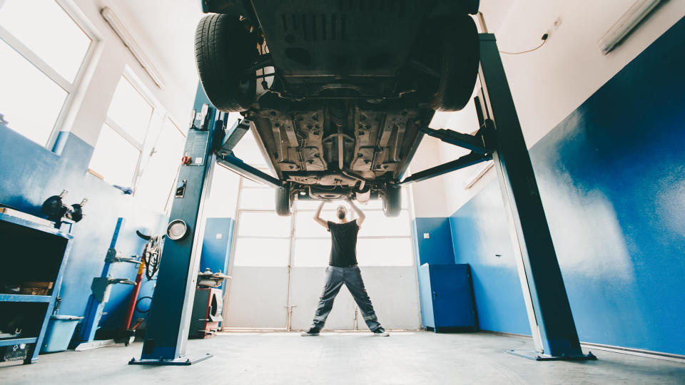 Young mechanic prepairing the car for inspection,distant view,bright light.