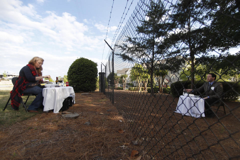 FILE - In this April 30, 2020 file photo, Justin and Crystal Craft enjoy their weekly dinner date on opposite sides of a fence surrounding the Park Springs senior community, where Justin runs the food and beverage department in Stone Mountain, Ga. Workers who agreed to live at a Georgia nursing home to keep its residents safe from the coronavirus will embrace their loved ones for the first time in more than two months on Saturday, June 13 as the home lifts a shelter-in-place restriction on its staff. (AP Photo/John Bazemore, File)