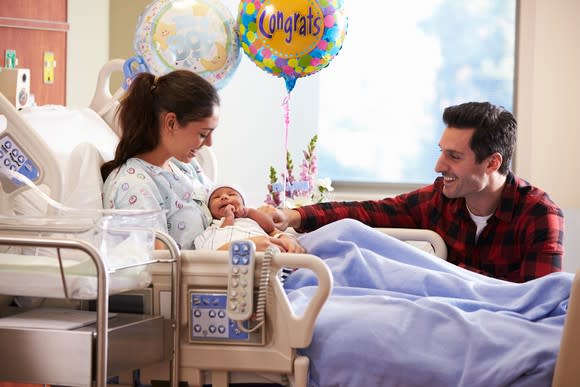 Infant in mom's arms in a hospital room with dad and baloons