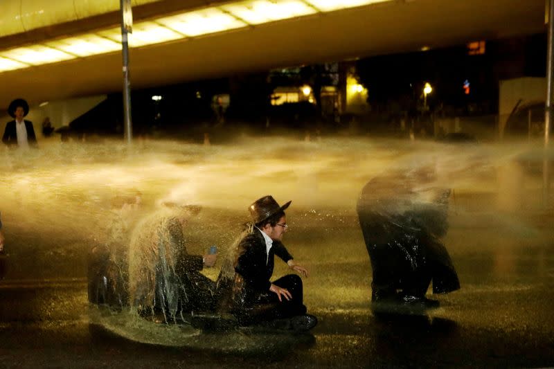 FILE PHOTO: Israeli ultra-Orthodox Jewish men sit as a water canon is activated during a protest