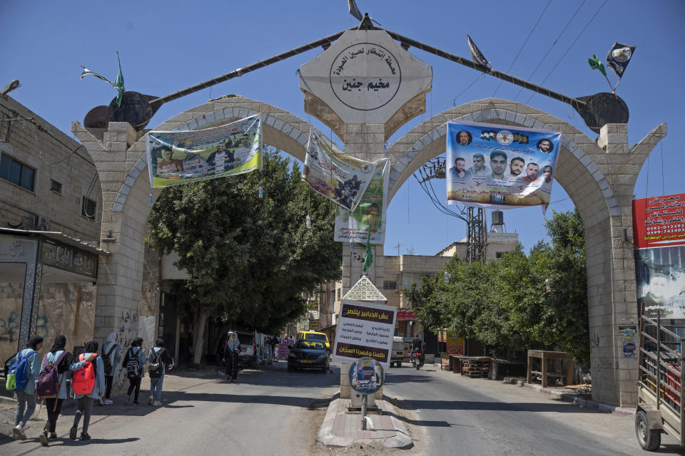 A banner, right, with pictures of the six Palestinian prisoners who escaped from an Israeli jail, their names and Arabic that reads, "the movement of Islamic Jihad, heroes of the Gilboa prison escape," hangs at the entrance of the Jenin refugee camp, in the West Bank city of Jenin, Wednesday, Sept. 8, 2021. Israel launched a massive manhunt in the country's north and the occupied West Bank after six Palestinian prisoners tunneled out of their cell and escaped overnight from a high security facility in an extremely rare breakout. (AP Photo/Nasser Nasser)