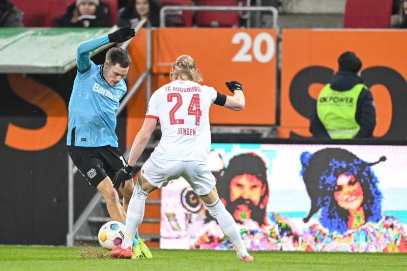 Leverkusen's Florian Wirtz (L) and Augsburg's Fredrik Jensen (R) battle for the ball during the German Bundesliga soccer match between FC Augsburg and Bayer Leverkusen at the WWK Arena. Harry Langer/dpa