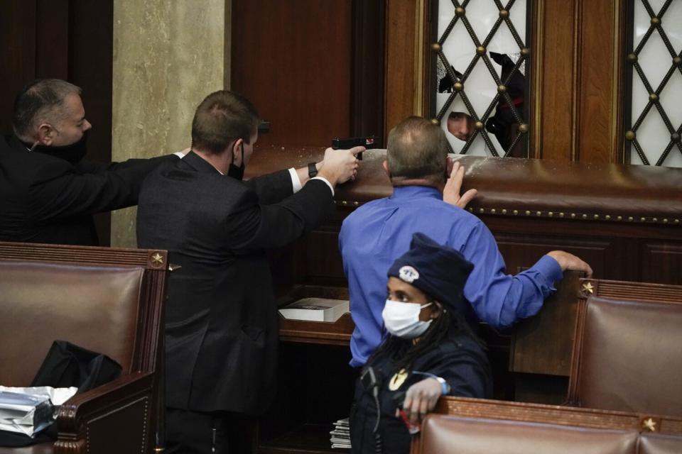 Police with guns drawn watch as rioters try to break into the House Chamber at the U.S. Capitol.