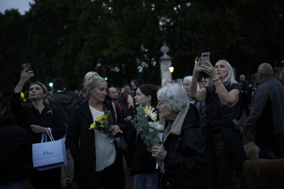 Mourners gather at dusk to commemorate Queen Elizabeth outside Buckingham Palace in London, Friday, Sept. 9, 2022. Queen Elizabeth II, Britain's longest-reigning monarch and a rock of stability across much of a turbulent century, died Thursday Sept. 8, 2022, after 70 years on the throne. She was 96. (AP Photo/Christophe Ena)