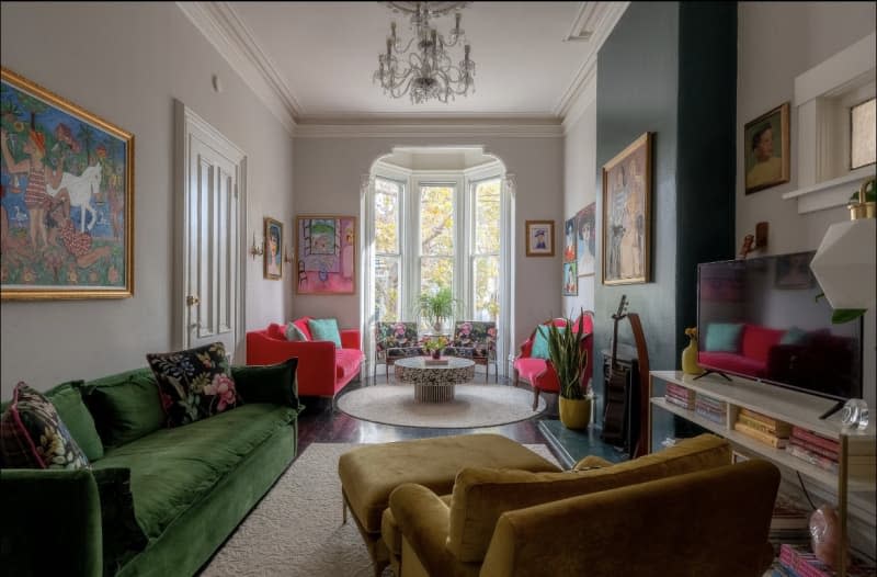 White living room with green velvet sofa and gold velvet armchair, bay window, and teal accent wall