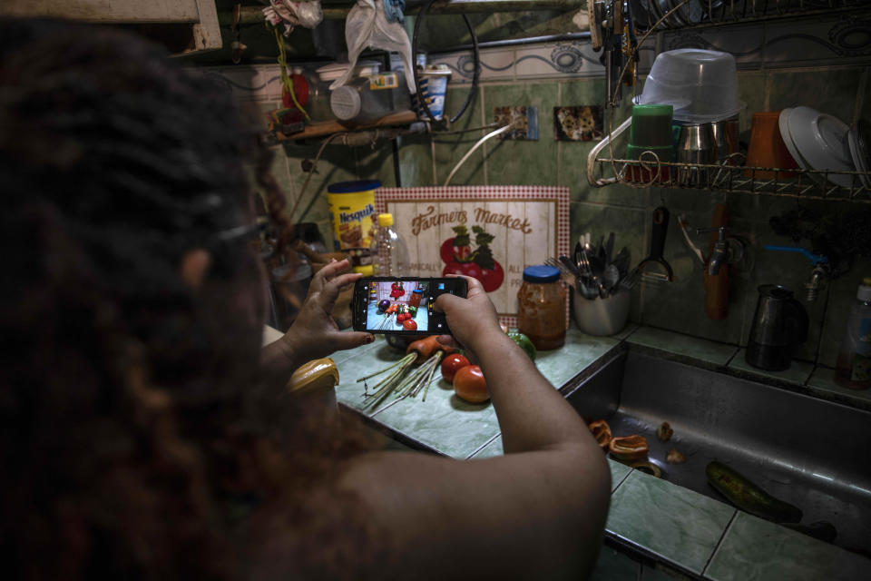 Contributor Yuliet Colon takes pictures of ingredients to upload to the “Recipes from the Heart” facebook page for her latest post, in her home in Havana, Cuba, Friday, April 2, 2021. Colon bought the few vegetables she could find at an agricultural market near her home, and used them to create something that she called “Cuban-style pisto manchego.” (AP Photo/Ramon Espinosa)