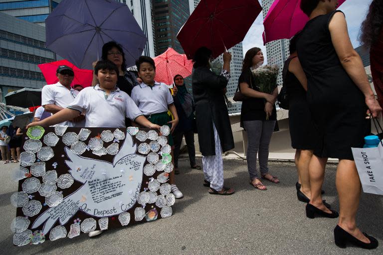 A boy (L) holds a collage of condolence messages while queuing to pay respects to Singapore's late former prime minister Lee Kuan Yew, near Parliament House, on March 25, 2015