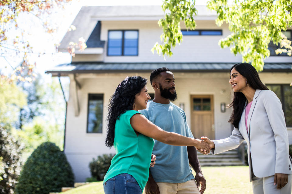 A couple shaking hands with a woman in front of a house