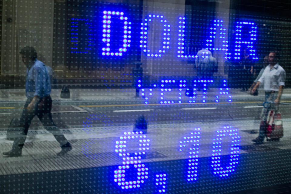 People are reflected on a sign displaying the rate of exchange between the Argentine peso and the U.S. dollar at a foreign exchange house in downtown Buenos Aires, Argentina, Tuesday, Jan. 28, 2014. Argentina announced on Friday it was relaxing restrictions on the purchase of U.S. dollars. The decision was forced by double-digit inflation and the hardest drop in the peso's value in over a decade. (AP Photo/Victor R. Caivano)