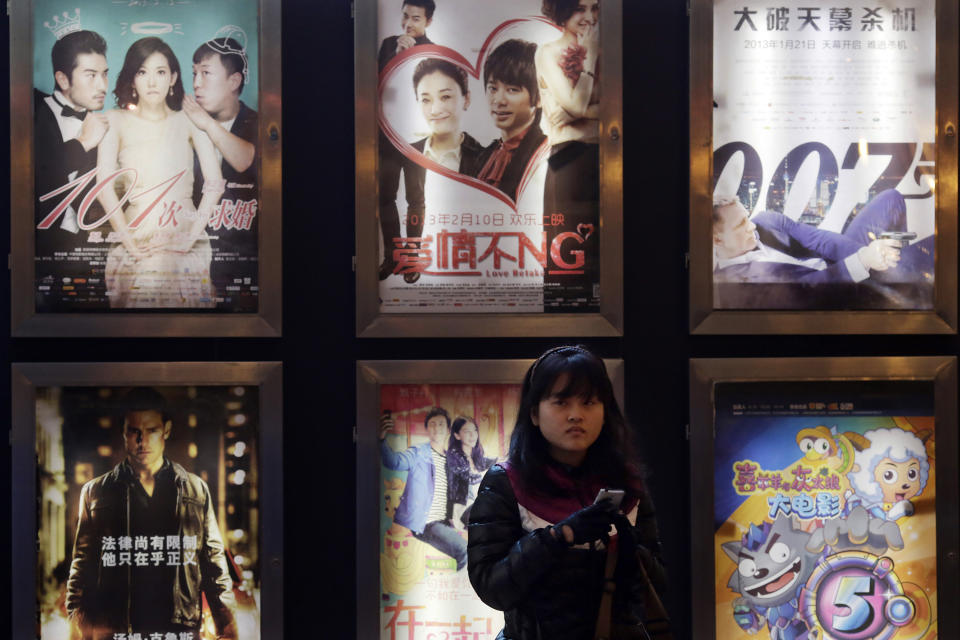 In this Wednesday Feb. 13, 2013 photo, a woman stands in front of the advertisements of Chinese and foreign films on showing at a movie theater in Shanghai, China. Tens of millions of film fanatics are entering theaters around Asia during the long Lunar New Year holiday, but Hollywood can’t count on them to boost the box office for its mostly serious Oscar nominees. Even with the Academy Awards buzz at a peak barely two weeks before the ceremony, patrons are opting for lighter fare. (AP Photo/Eugene Hoshiko)