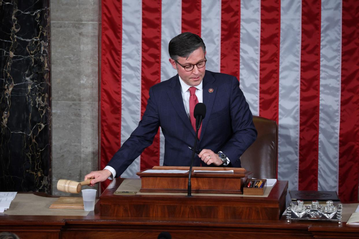 A boring-looking bespectacled man reaches for the gavel in the U.S. House chamber.
