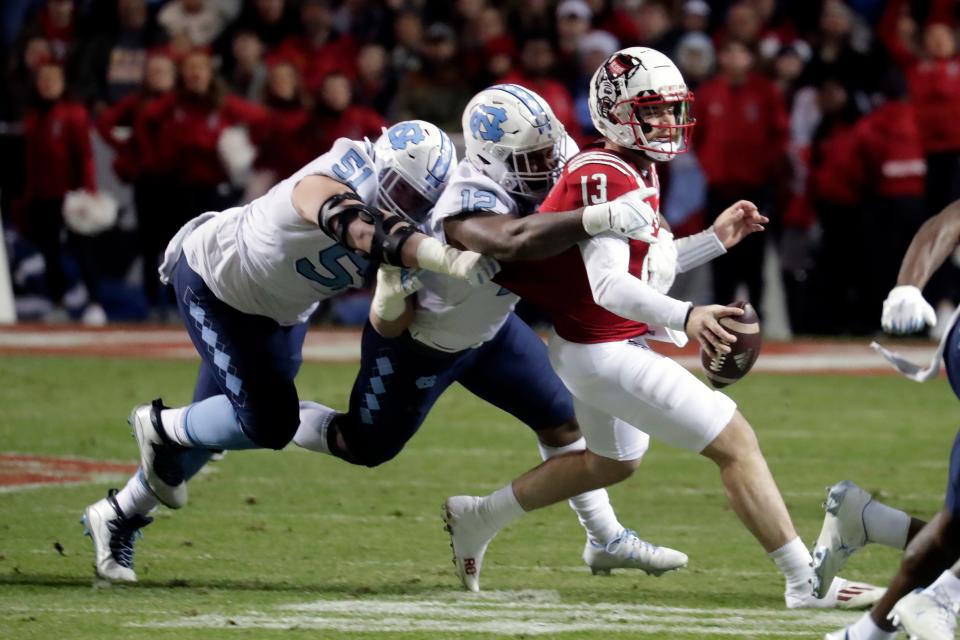 North Carolina State quarterback Devin Leary (13) is tackled by North Carolina defensive lineman Raymond Vohasek (51) and linebacker Tomon Fox (12) during the first half of an NCAA college football game Friday, Nov. 26, 2021, in Raleigh, N.C. (AP Photo/Chris Seward)