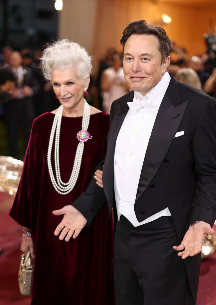 Two individuals posing together, one in a velvet gown with pearls, the other in a formal tuxedo