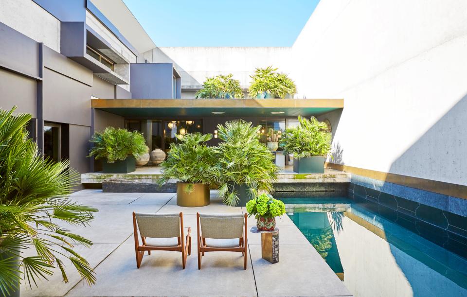 On the terrace, a marble-and-brass side table by Vincenzo De Cotiis stands alongside a pair of vintage chairs. The home’s exterior is made of concrete, painted wood, and brass.