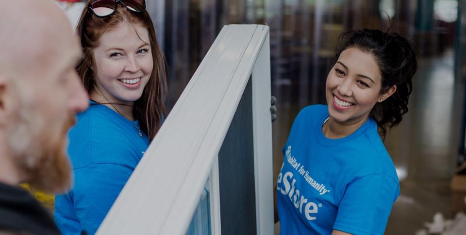 Three Habitat ReStore employees in blue shirts carrying a door.