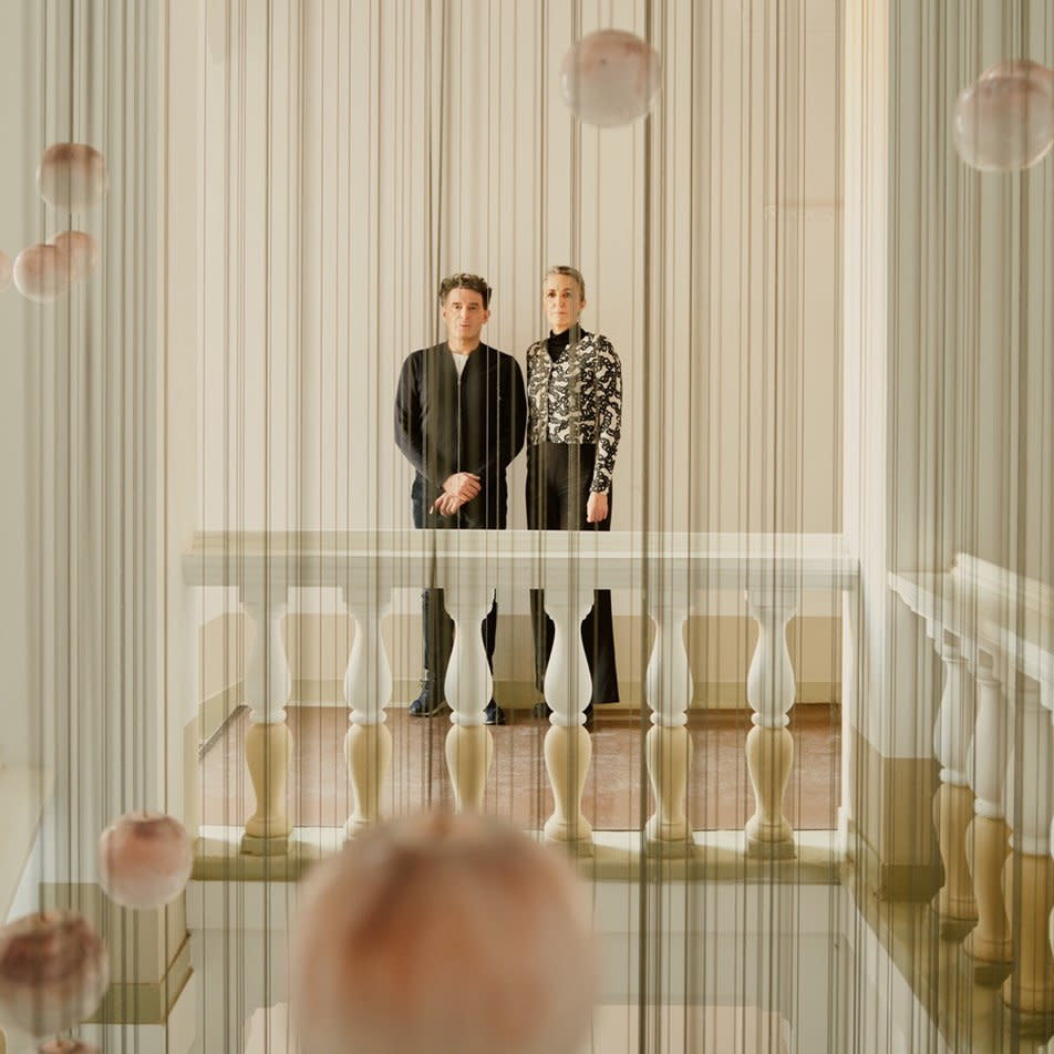  Grüntuck Ernst Architects pose behing several hanging ornaments at the top of an ornate staircase in the Wilmina Hotel.