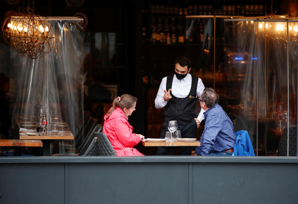 A waiter wearing a face mask serves customers in a restaurant, following the outbreak of the coronavirus disease (COVID-19), in St. Albans, Britain, October 8, 2020.  REUTERS/Peter Cziborra