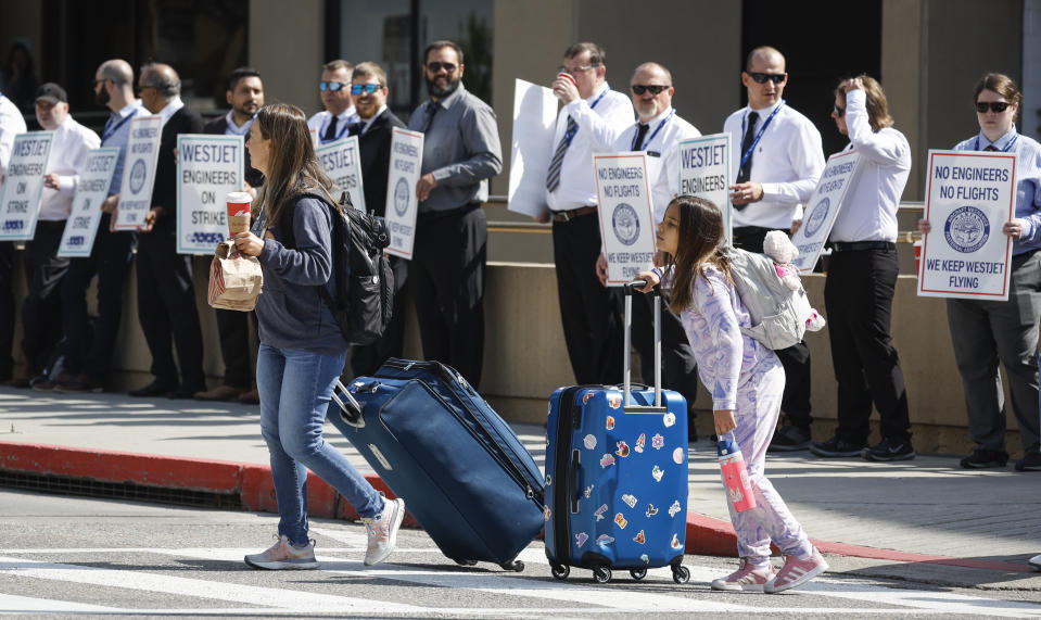 Passengers make their way past WestJet airplane mechanics as they stand in a the picket line at Calgary International Airport in Calgary, Saturday, June 29, 2024.THE CANADIAN PRESS/Jeff McIntosh