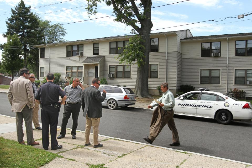 In this 2014 file photo, Providence police detectives stand guard as the jury in the trial of 18-year-old Quandell Husband visits various locations near the site of a triple murder at 151 General St., seen in the background.