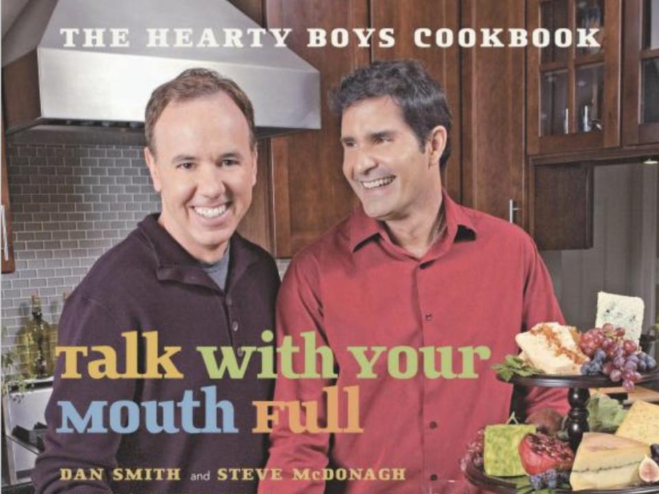 Dan and Steve smiling in a kitchen full of food with the printed words "Eat With Your Mouth Full."