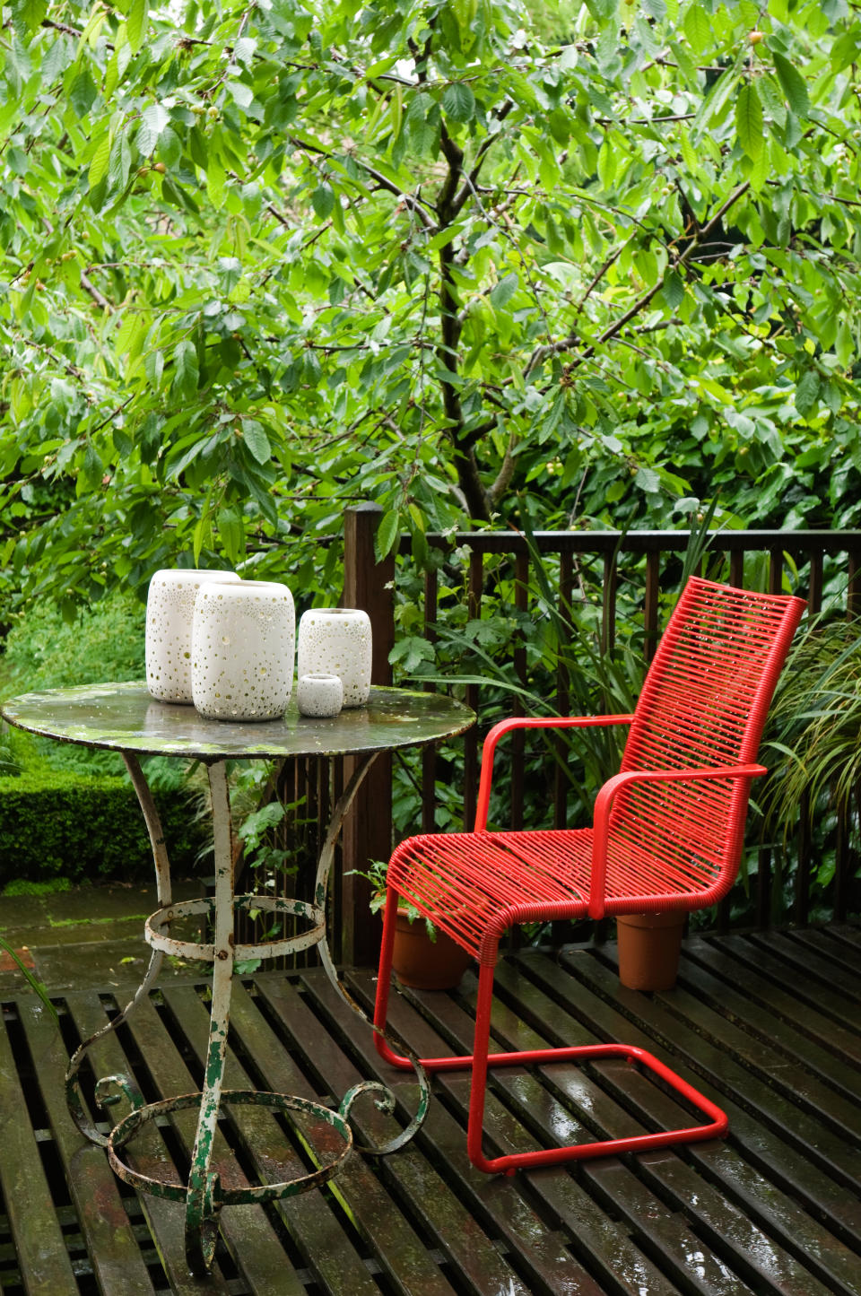 A small veranda with a small glass table and red metal chairs