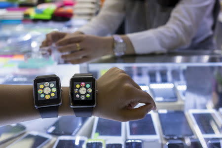 A salesman poses with two Apple Watch look-alike devices, made by a Chinese manufacturer, at a mall selling electronic products in China's southern city of Shenzhen, April 8, 2015. REUTERS/Tyrone Siu