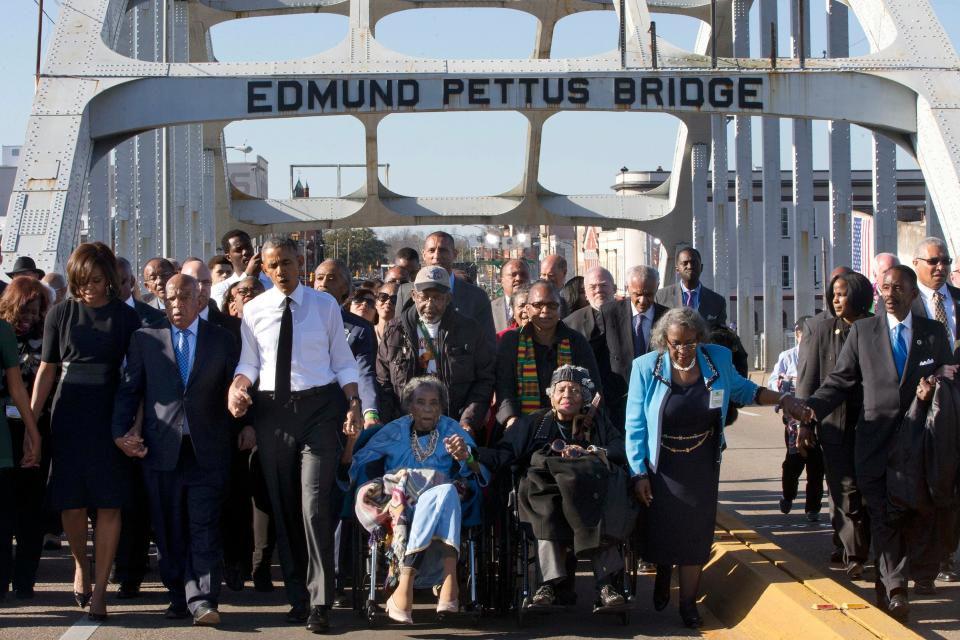 In this March 7, 2015, file photo, singing "We Shall Overcome," President Barack Obama, third from left, walks holding hands with Amelia Boynton, who was beaten during Bloody Sunday, as they and the first family and others including Rep. John Lewis, D-Ga, left of Obama, walk across the Edmund Pettus Bridge in Selma, Alabama, for the 50th anniversary of Bloody Sunday, a landmark event of the civil rights movement. Some residents in Selma are among the critics of a bid to rename the historic bridge where voting rights marchers were beaten in 1965.