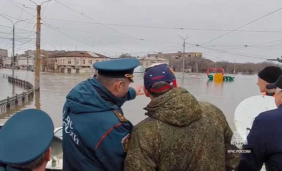 In this grab taken from a video released by the Russian Emergency Ministry Press Service on Sunday, April 7, 2024, Russian Emergency Situations Minister Alexnader Kurenkov, center left, back to a camera, stands on a boat observing water levels, in Orsk, Russia. State media say Russia's government has declared the situation in flood-hit areas in the Orenburg region a federal emergency. The floods, caused by rising water levels in the Ural River, forced over 4,000 people, including over 800 children, to evacuate, the regional government said. (Russian Emergency Ministry Press Service via AP)