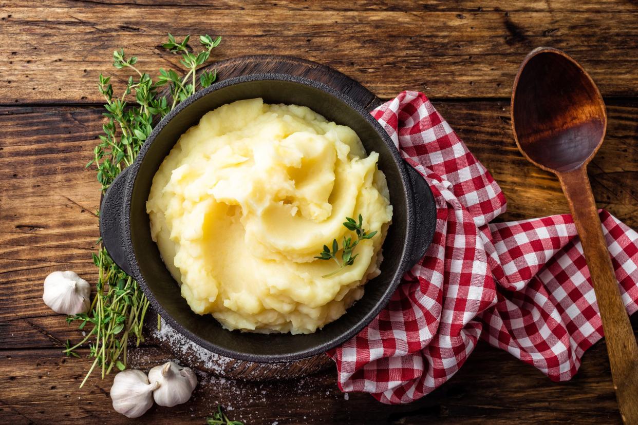 Roasted garlic mashed potatoes in a cast iron pot with a red checkered napkin and a wooden spoon on a rustic wooden table