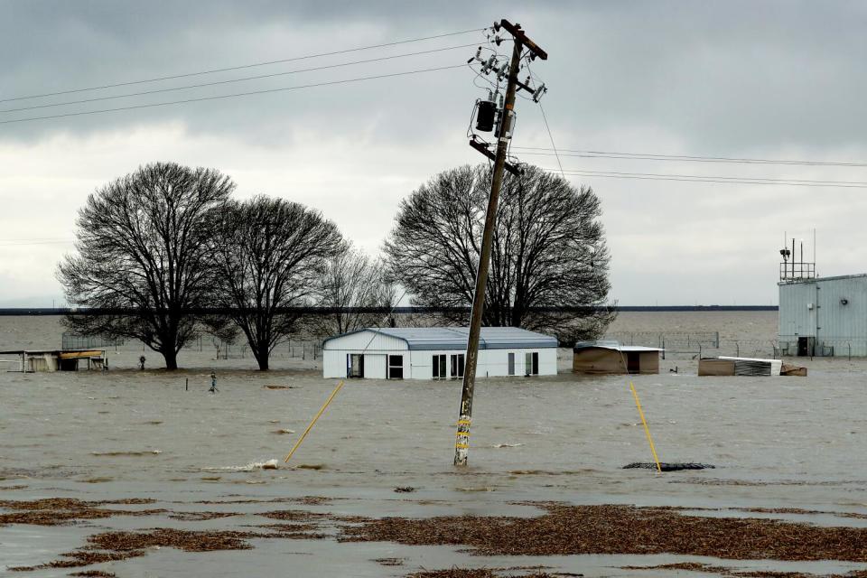 Floodwaters surround a house structure. A telephone pole leans from the water at the center.