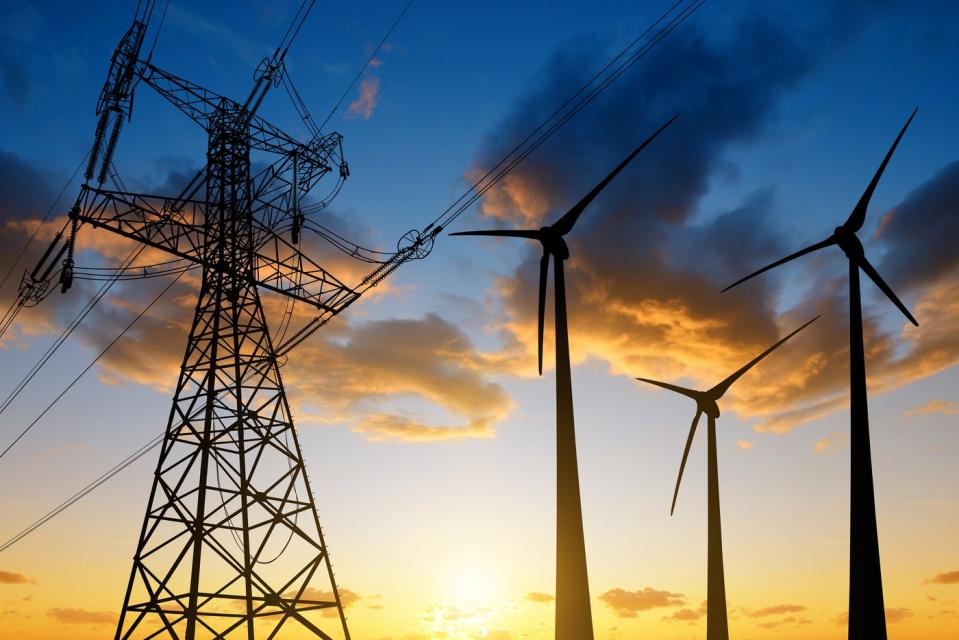 Three wind turbines next to an electrical tower, with the sun rising in the background.