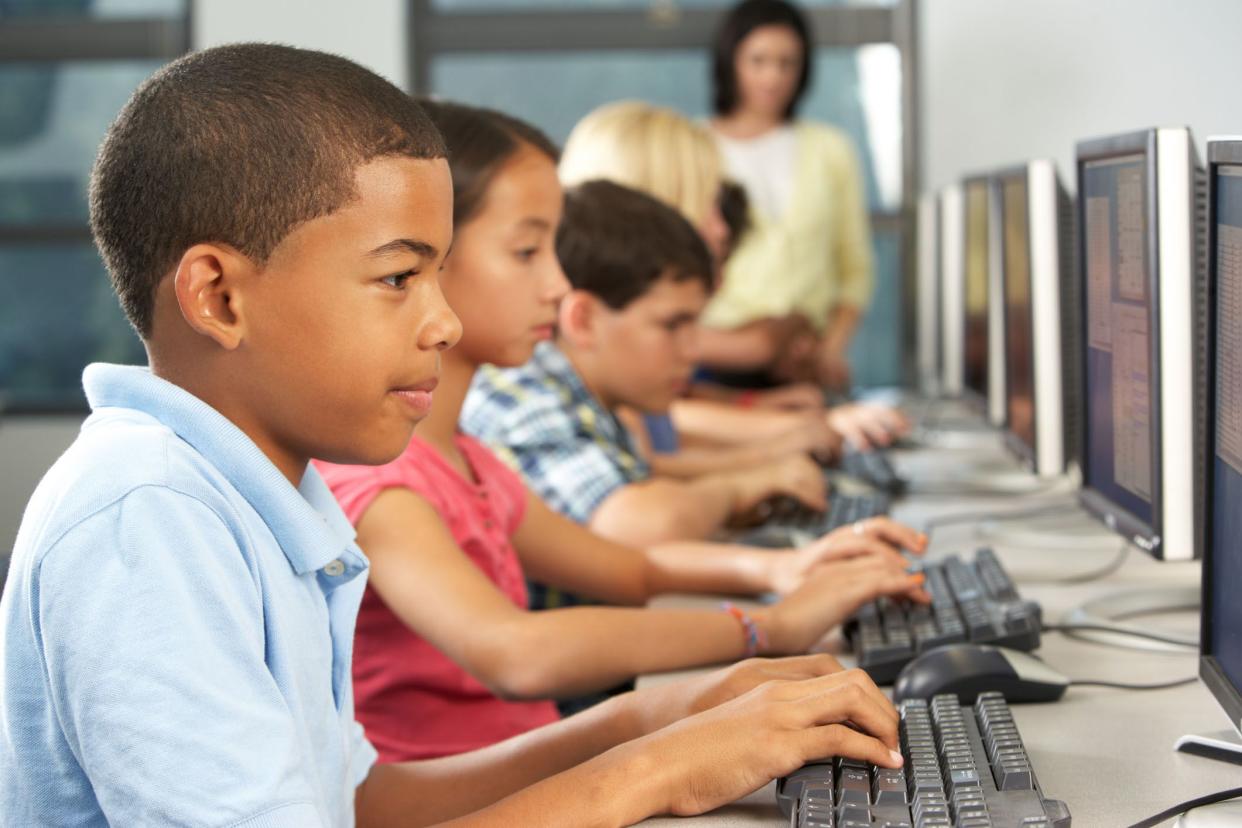 students typing on computers in class; teacher supervising in background