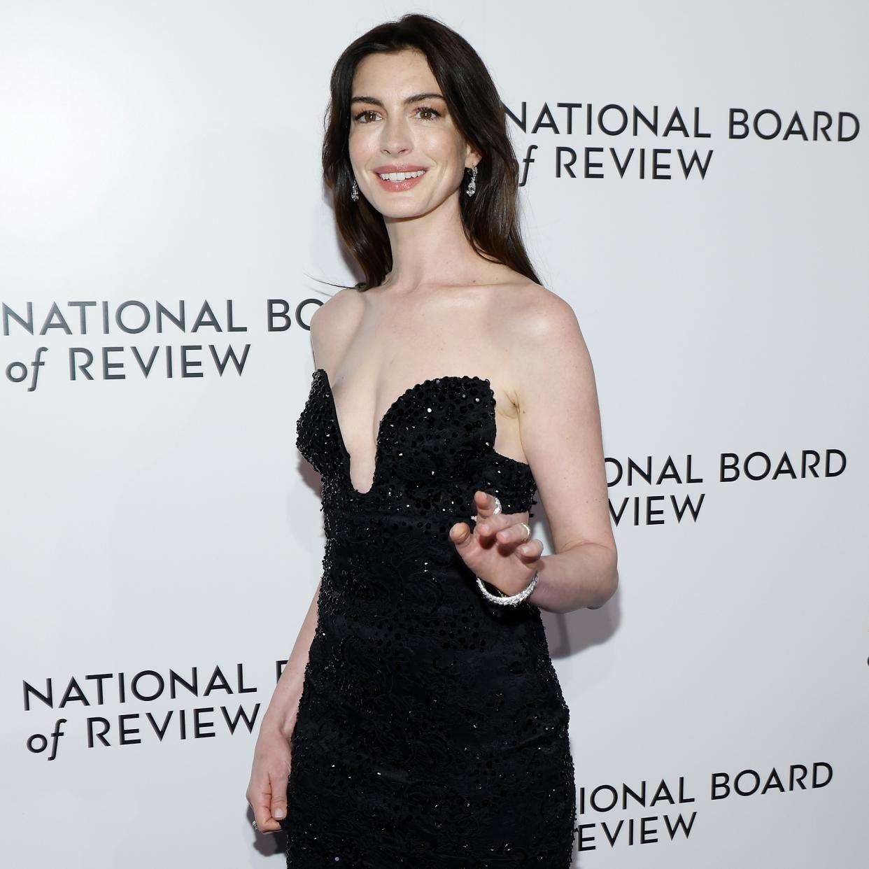  Anne Hathaway is wearing a sleeveless black dress smiling and waving to the camera. . 