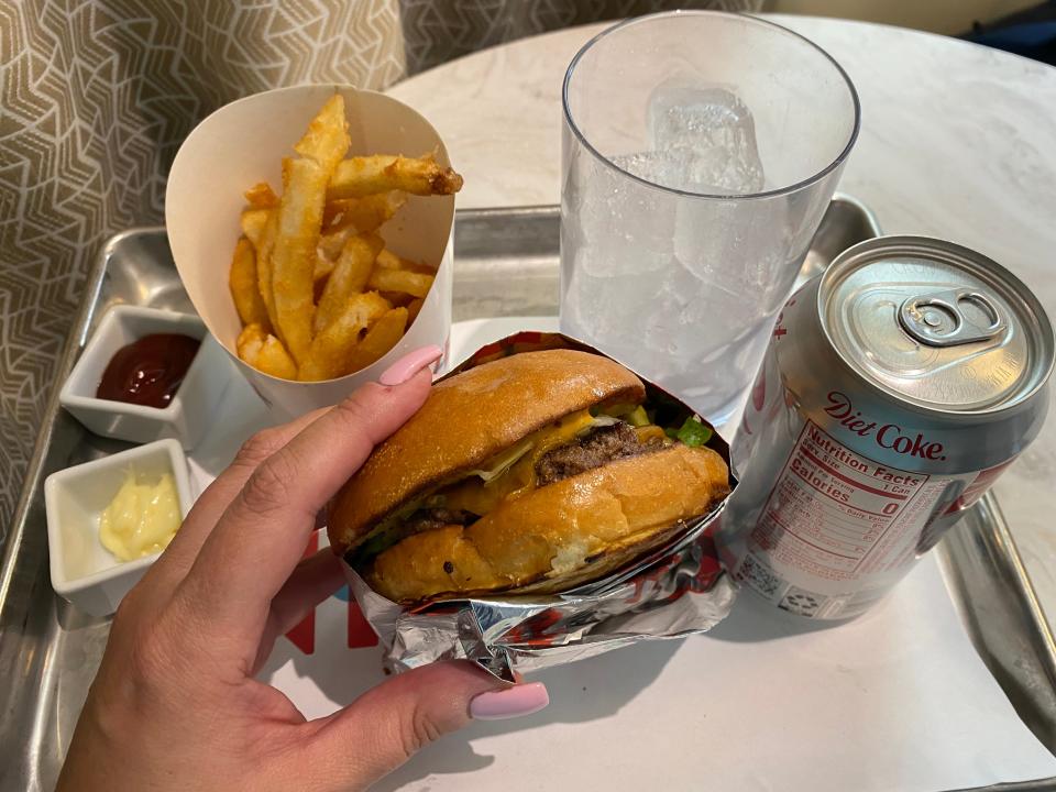 A burger, fries, glass of ice, and diet coke can on a tray