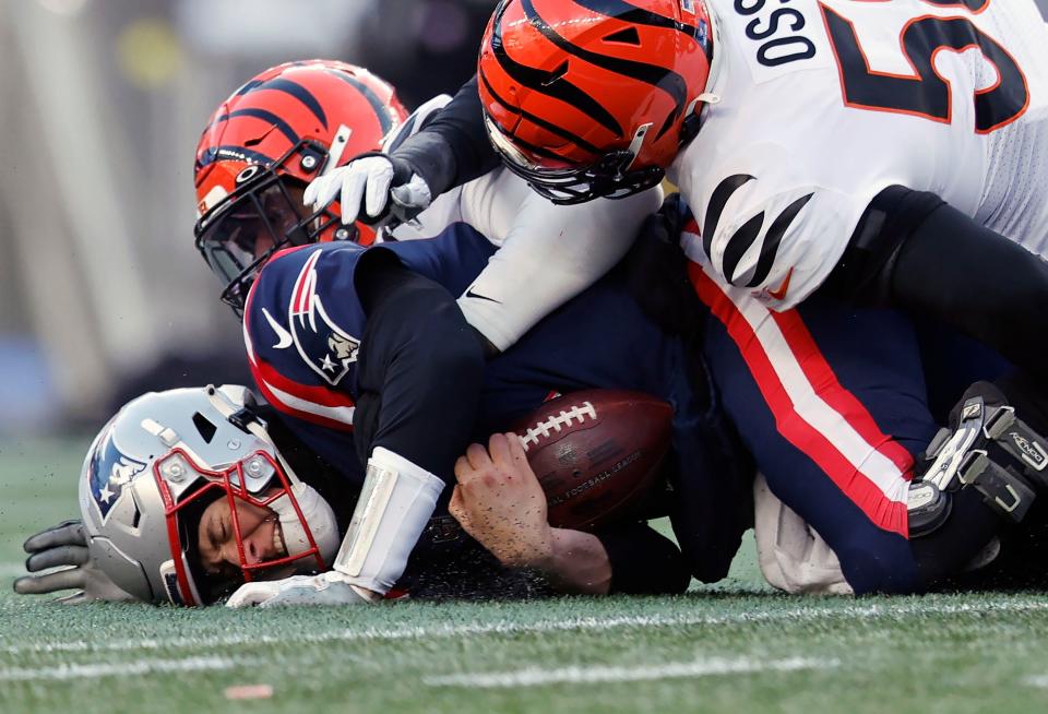 Patriots quarterback Mac Jones, left, holds the ball as he hits the ground after being tackled by Bengals defensive end Joseph Ossai, right, during the second half of Saturday's game.