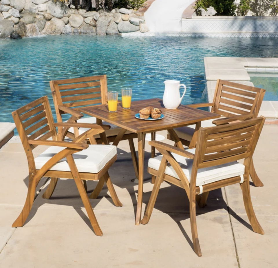 Mercury Row 4-Person Dining Set in brown wood against blue pool and stones (Photo via Wayfair)