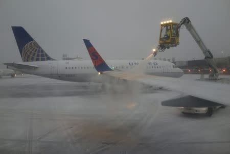 A Sun Country Airlines plane's wing is de-iced as a United Airlines plane waits at the de-icing station during a snowstorm at Logan International Airport in Boston, Massachusetts, United States December 29, 2015. REUTERS/Lucy Nicholson