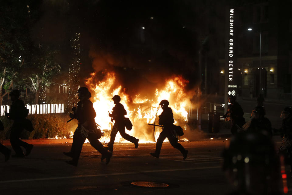 Police officers rush past a burning police vehicle to disperse protesters during a protest over the death of George Floyd Saturday, May 30, 2020, in Los Angeles. Floyd died in police custody Monday in Minneapolis. (AP Photo/Jae C. Hong)