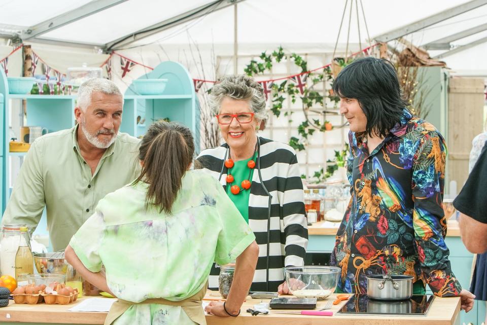 Four individuals in a cooking tent, engaging in conversation with a baking counter and equipment around them