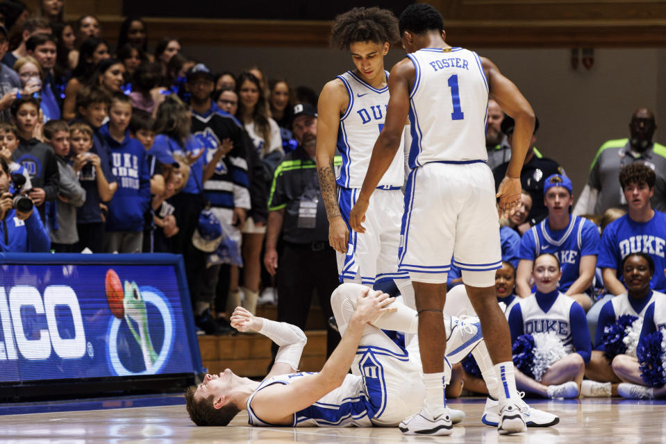 Duke's Kyle Filipowski, bottom, holds his leg after an injury while teammates Tyrese Proctor, top left, and Caleb Foster (1) look down during the first half of an NCAA college basketball game against Bucknell in Durham, N.C., Friday, Nov. 17, 2023. (AP Photo/Ben McKeown)