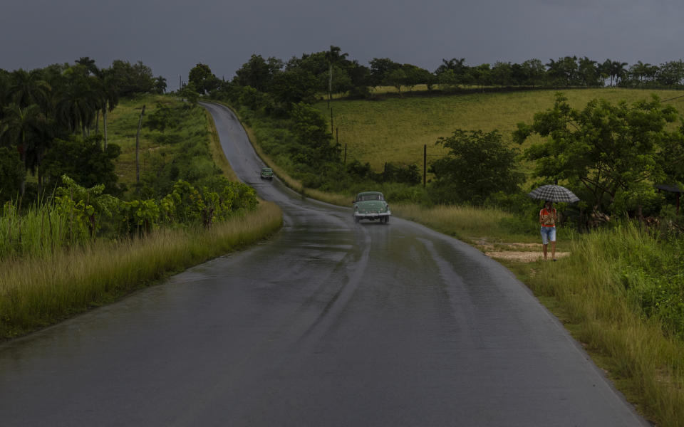 A woman walks on the shoulder of a road using an umbrella as protection against rains brought on by Hurricane Ida, in Guanimar, Artemisa province, Cuba, Saturday, Aug. 28, 2021. (AP Photo/Ramon Espinosa)