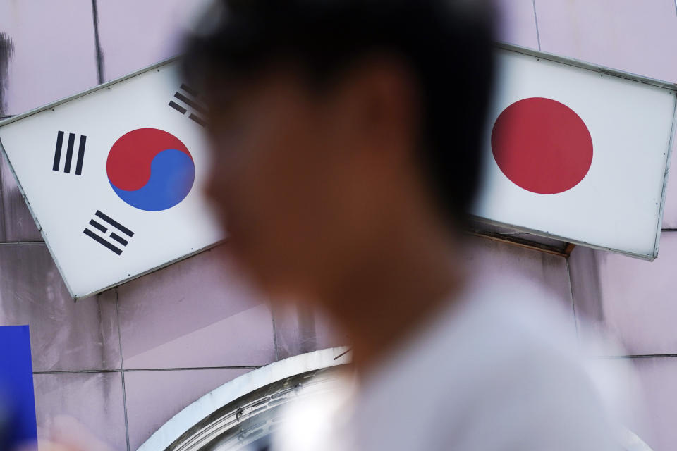 In this Aug. 13, 2019 photo, a man walks past an advertisement featuring Japanese and South Korean flags at a shop in Shin Okubo area, in Tokyo. South Korea and Japan have locked themselves in a highly-public dispute over history and trade that in a span of weeks saw their relations sink to a low unseen in decades. This area is known for Korean restaurants and stores selling K-pop merchandise.(AP Photo/Eugene Hoshiko)