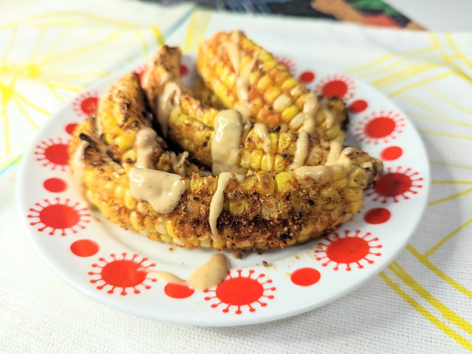 red and white plate with corn ribs on it drizzled with a tan sauce