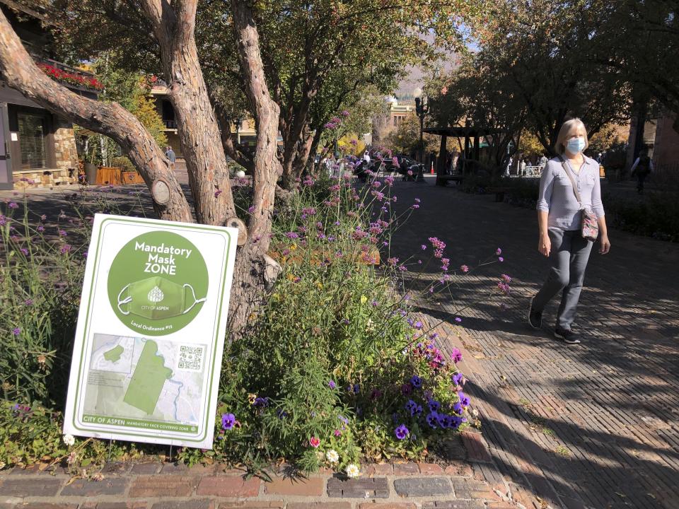 In this Oct. 3, 2020 photo, a pedestrian walks past one of the many signs along the mandatory mask zone in the downtown area in Aspen, Colo. Aspen has taken numerous precautionary measures during the coronavirus pandemic, including mask mandates, occupancy limits in shops and restaurants, and social distancing. (AP Photo/John Marshall)